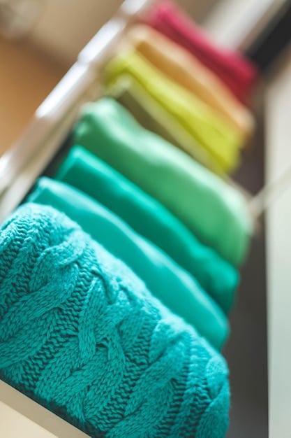 Close-up shot of a well-organized capsule wardrobe, focusing on the textures and colors of the garments. The wardrobe includes items like a white button-down shirt, black trousers, a denim jacket, and a simple dress. The image emphasizes the quality and versatility of each item.