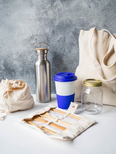 A close-up shot of various reusable containers and utensils (water bottle, coffee mug, cloth bags, metal straws, beeswax wraps) arranged on a wooden surface, showcasing different types of sustainable alternatives.
