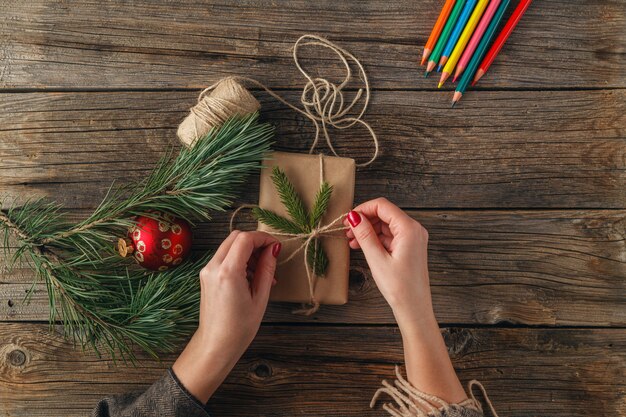 A person wrapping a gift with brown kraft paper and tying it with twine, adorned with a sprig of greenery. The focus is on the simplicity and natural materials used in sustainable gift wrapping.