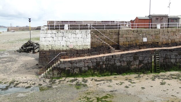 A before-and-after shot of a seawall construction project. The 'before' image shows a heavily eroded coastline, while the 'after' image shows a newly constructed seawall protecting nearby buildings.